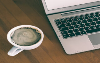 cup of coffee next to laptop on desk